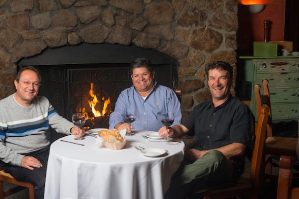 three owners sitting at table in front of fireplace