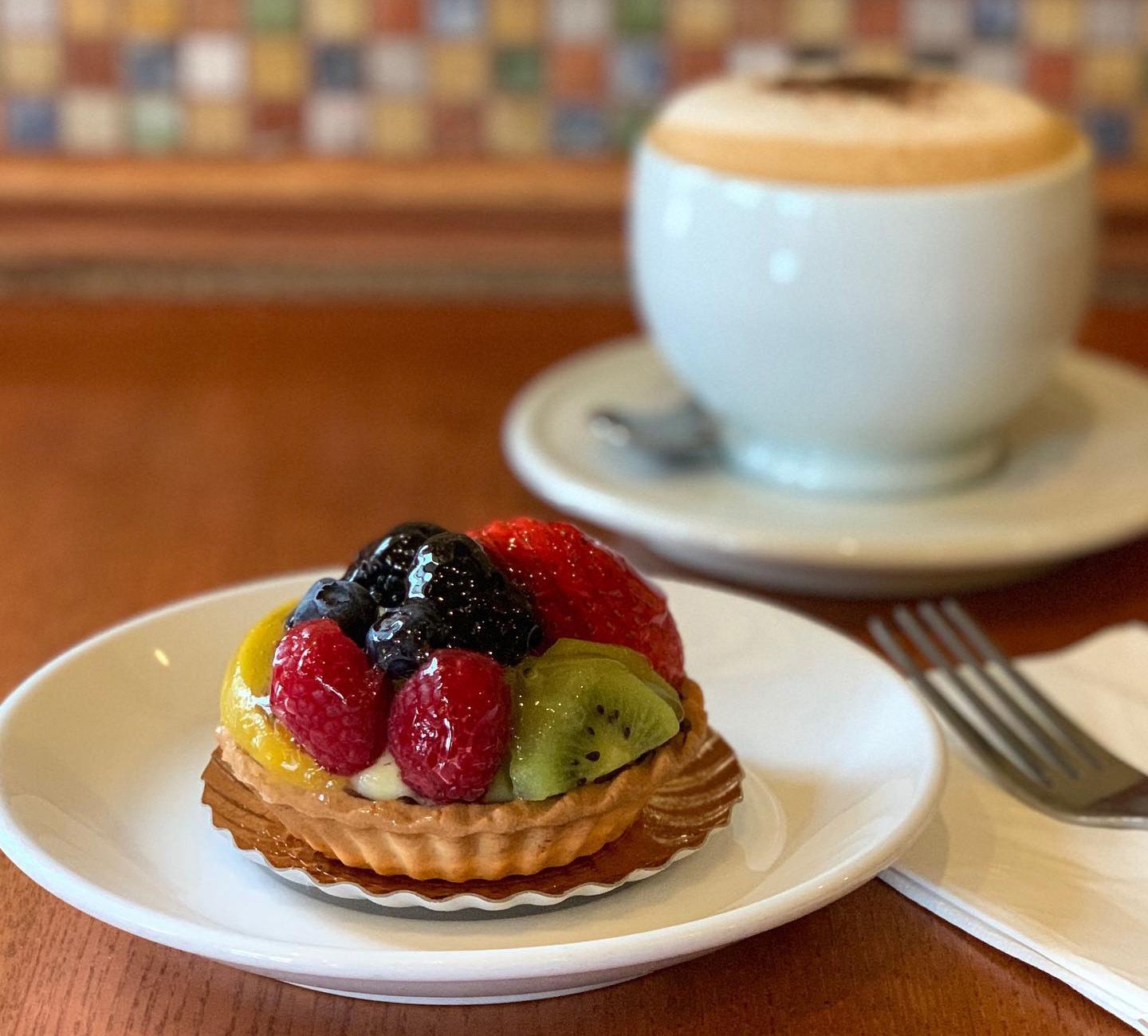fruit tart on plate with cappuccino in background