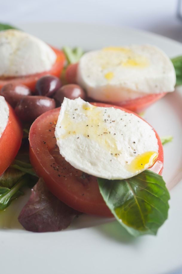 caprese salad with tomatoes, fresh mozzarella, olives, and basil leaves